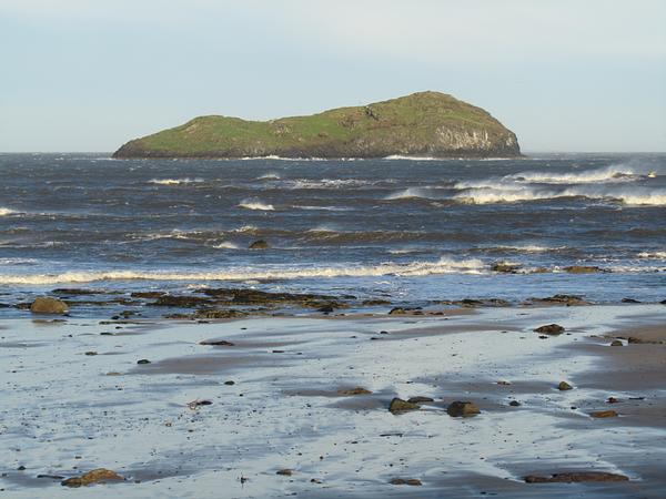 Craigleith island, covered in green vegetation, sits on a stormy sea